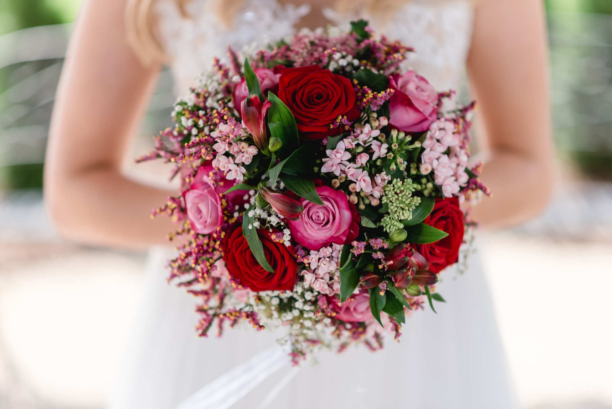 eine Braut, die einen Strauß roter und rosa Rosen hält.
