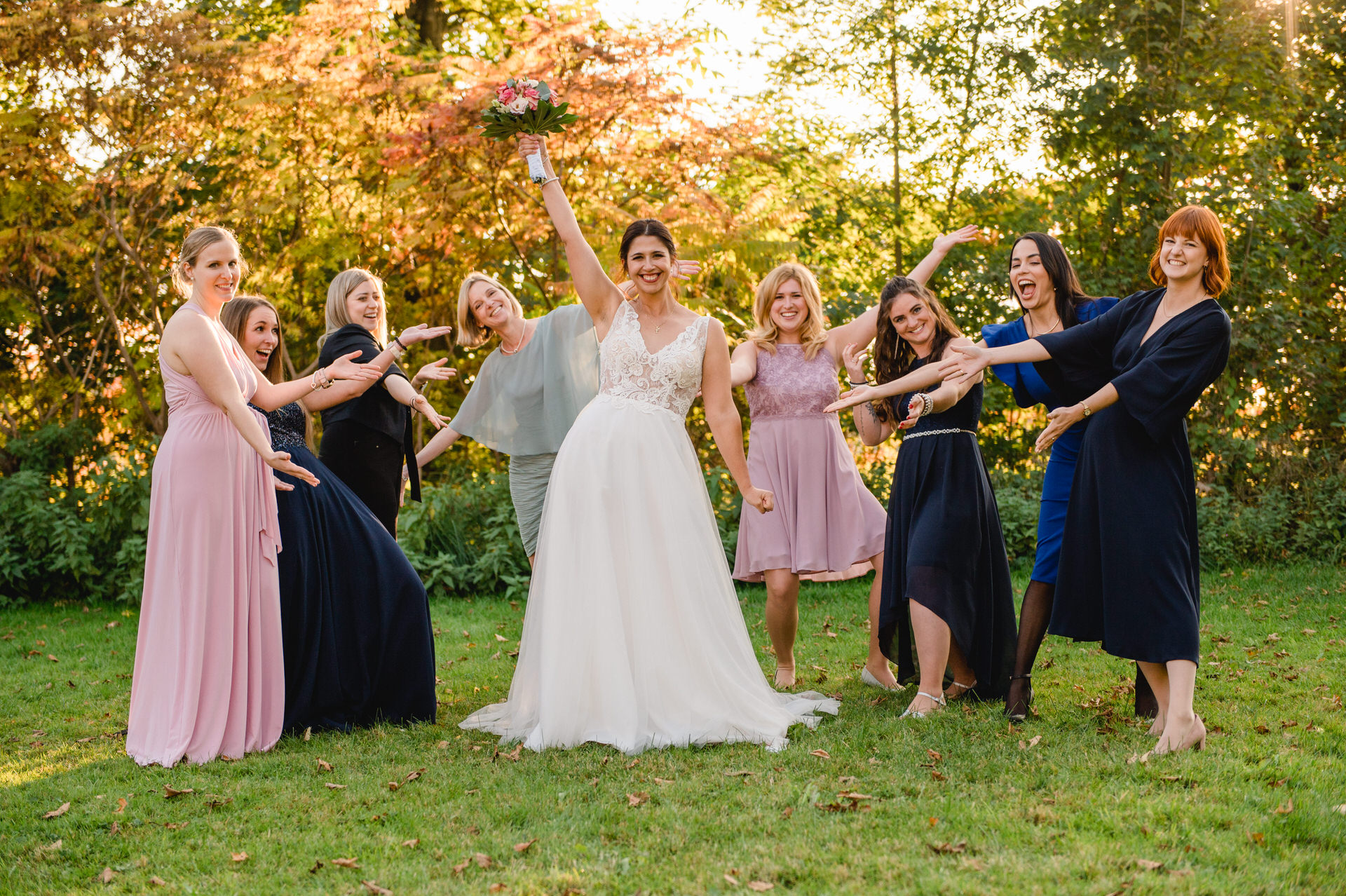 Eine Braut und ihre Brautjungfern halten ihre Blumensträuße in die Luft.