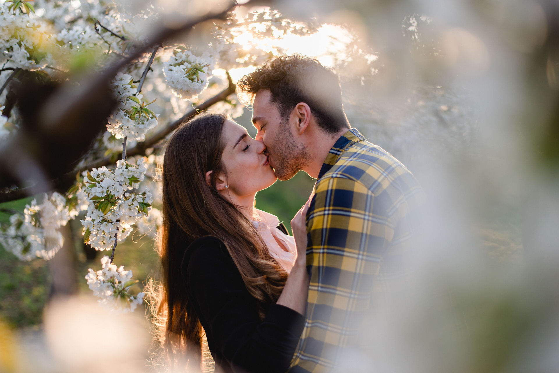 Ein Mann und eine Frau küssen sich vor einem blühenden Baum.