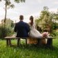 Eine Braut und ein Bräutigam sitzen auf einer Bank im Gras.