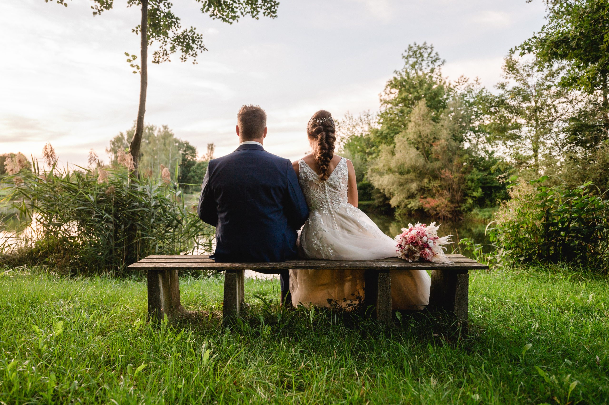 Eine Braut und ein Bräutigam sitzen auf einer Bank im Gras.