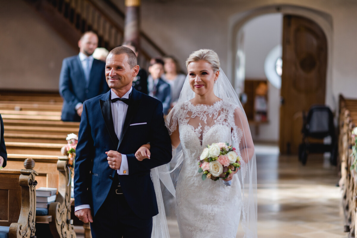 Janina_Daniel_Ettringen_00008 Ein Brautpaar, das den Gang einer Kirche hinuntergeht.
