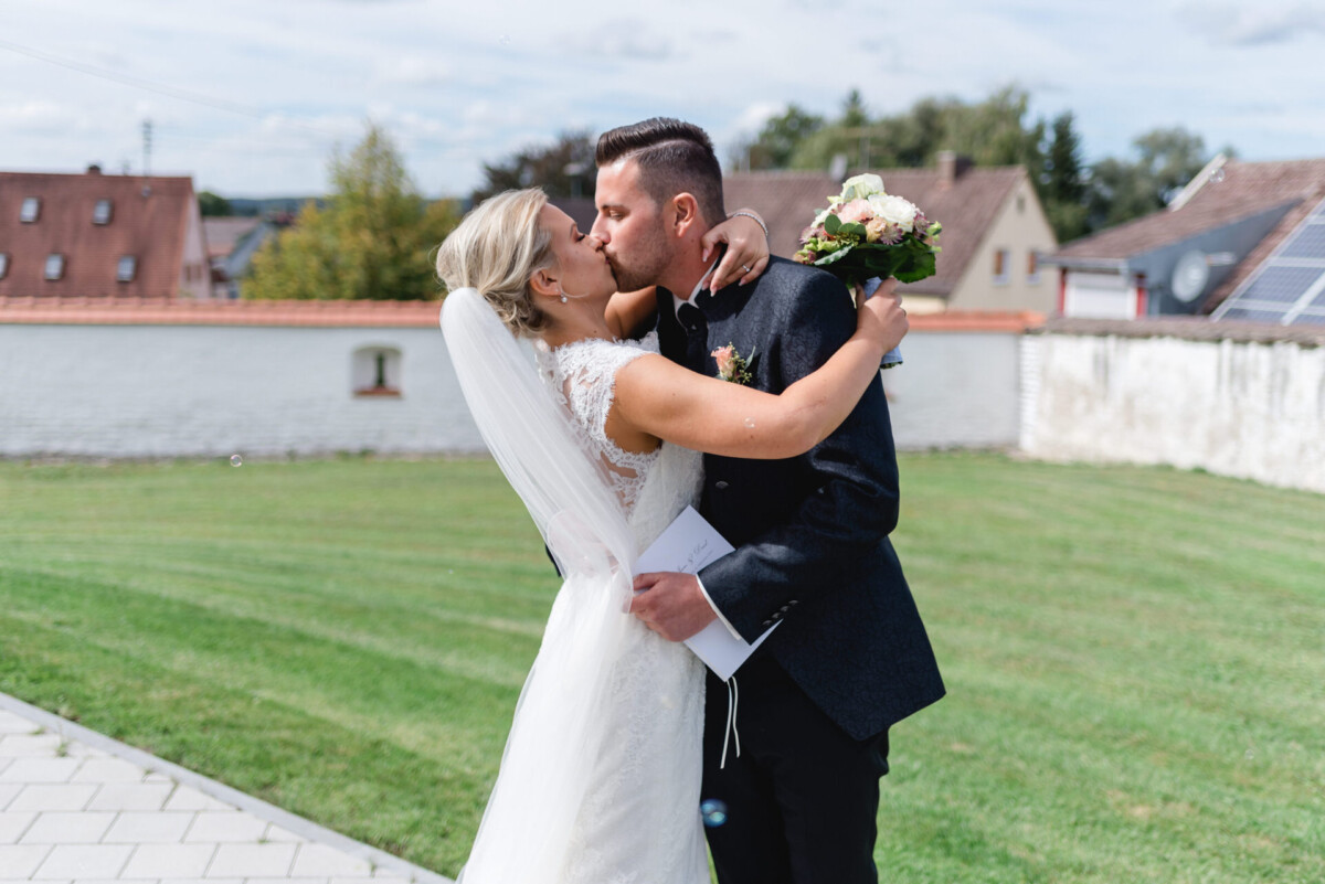 Janina_Daniel_Ettringen_00017 ein Brautpaar, das sich auf einem Feld küsst.