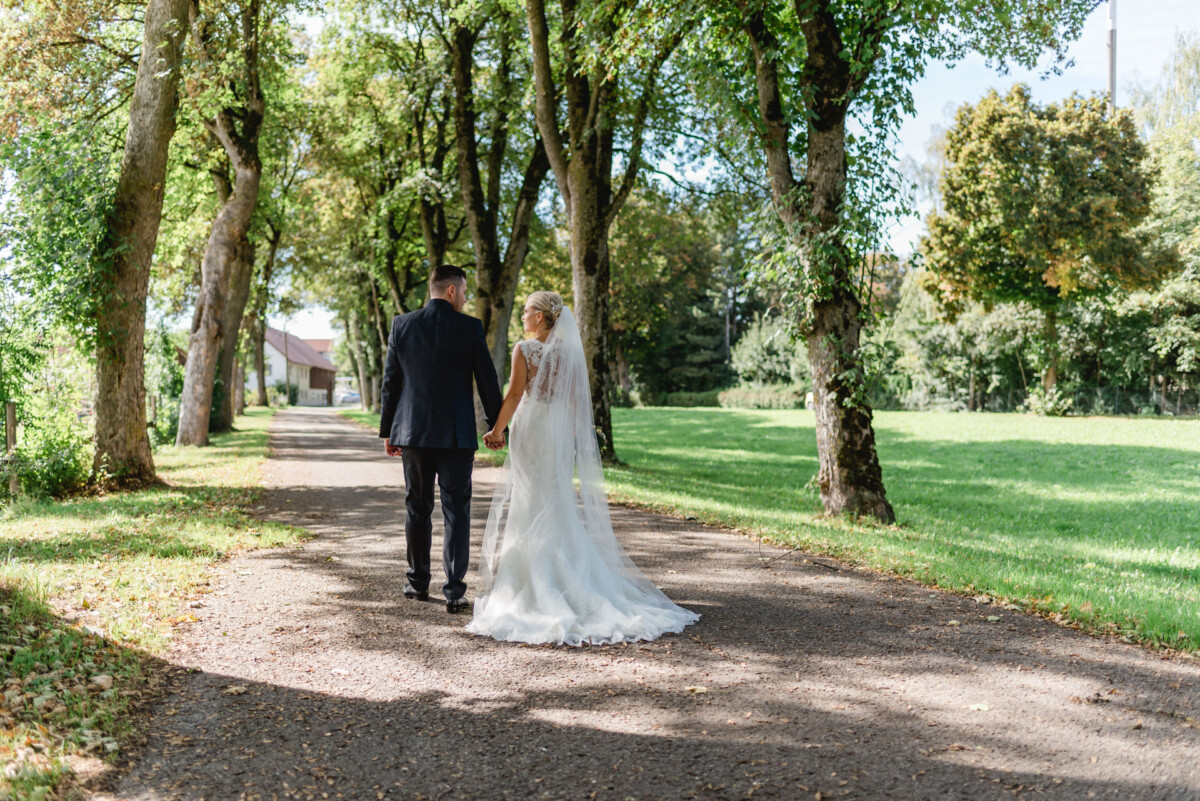 Janina_Daniel_Ettringen_00018 eine Braut und ein Bräutigam, die einen Weg in einem Park hinuntergehen.