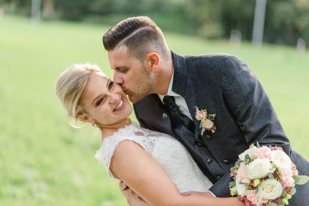 Janina_Daniel_Ettringen_00027 ein Brautpaar, das sich auf einem Feld küsst.