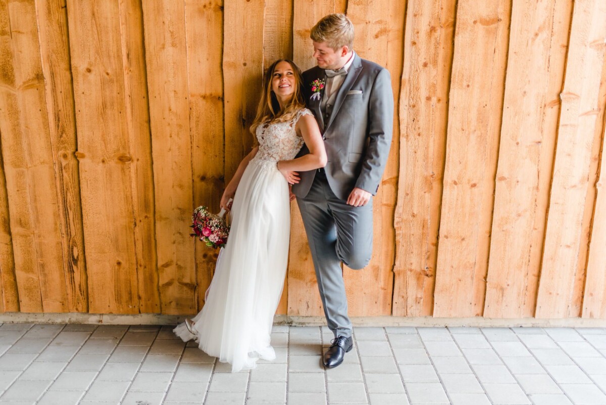 Julia_Marco_Donauwoerth_00002 Eine Braut und ein Bräutigam, die sich an eine Holzwand lehnen.