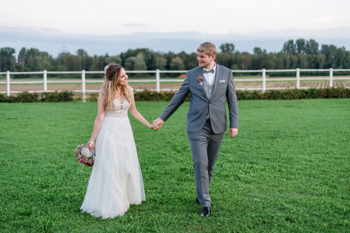 Julia_Marco_Donauwoerth_00021 Eine Braut und ein Bräutigam halten Händchen in einem Feld