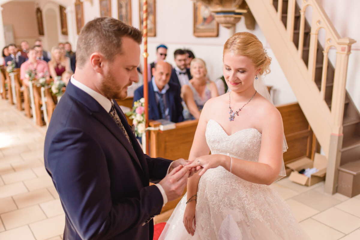 Natalie_Willi_Sulzemoos_00010 Ein Mann und eine Frau, die während einer Hochzeitszeremonie Händchen halten.