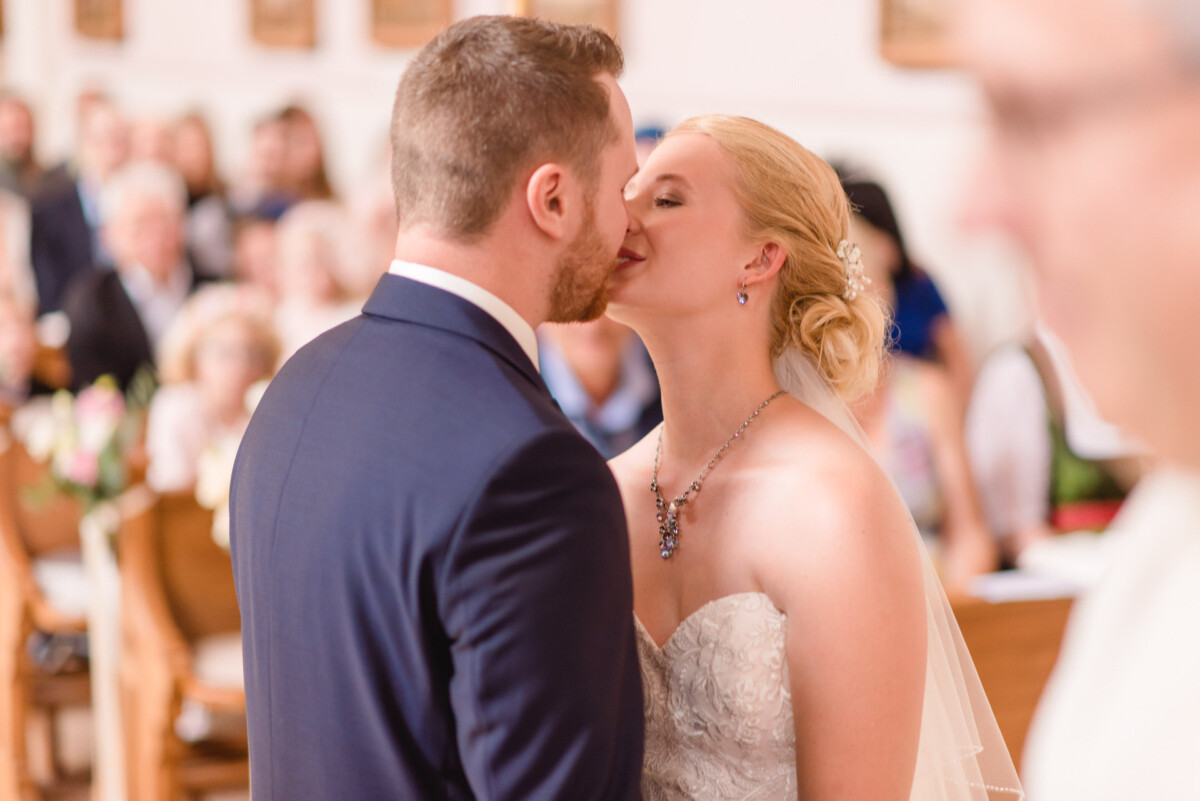 Natalie_Willi_Sulzemoos_00013 ein Brautpaar, das sich vor einer Menschenmenge küsst.