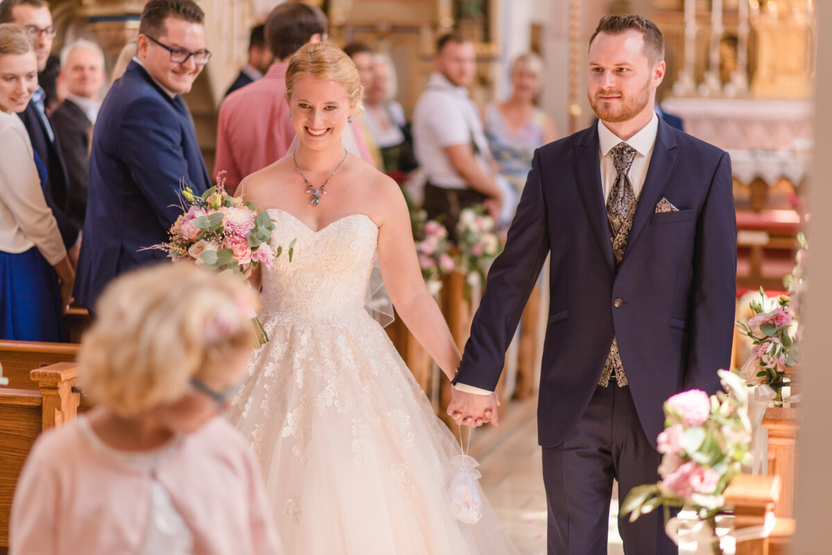 Natalie_Willi_Sulzemoos_00019 Ein Brautpaar, das den Gang einer Kirche hinuntergeht.