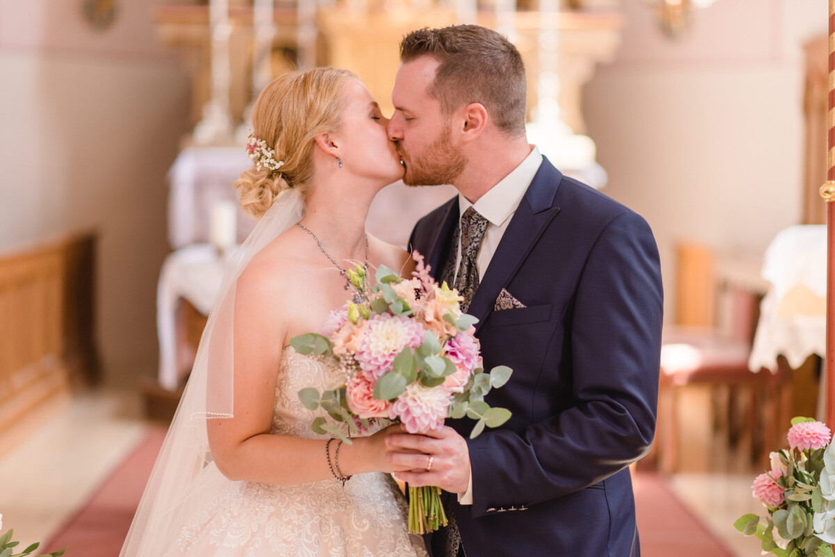 Natalie_Willi_Sulzemoos_00023 ein Brautpaar, das sich in einer Kirche küsst.