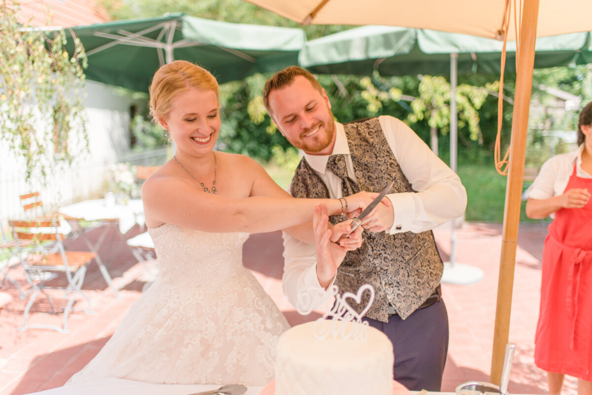 Natalie_Willi_Sulzemoos_00025 Ein Mann und eine Frau schneiden eine Hochzeitstorte an.