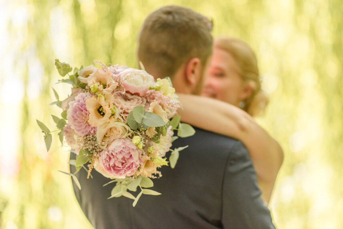 Natalie_Willi_Sulzemoos_00031 Eine Braut und ein Bräutigam, die sich vor einem Baum umarmen.