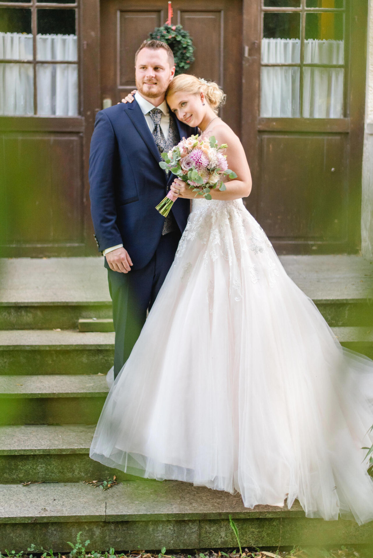 Natalie_Willi_Sulzemoos_00032 Eine Braut und ein Bräutigam stehen auf den Stufen eines Hauses.