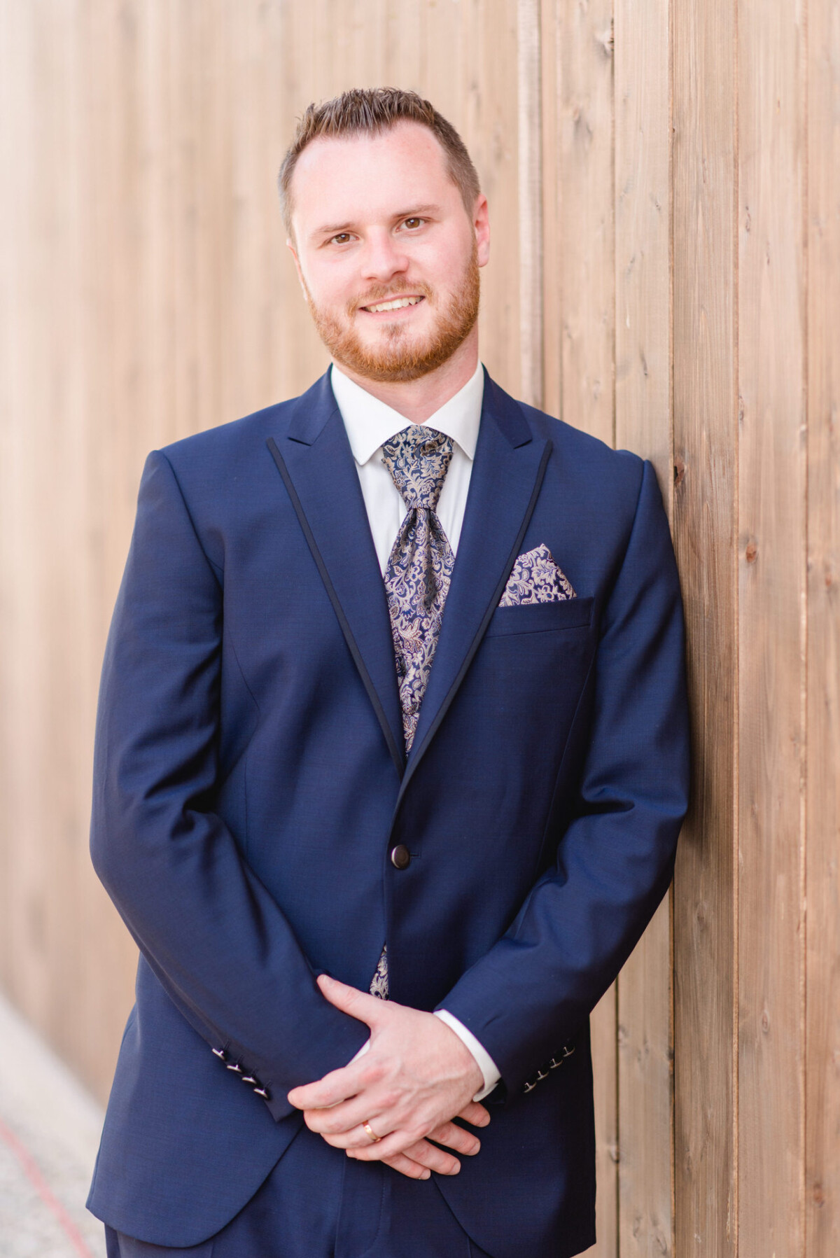 Natalie_Willi_Sulzemoos_00035 Ein Mann im Anzug lehnt an einer Holzwand.