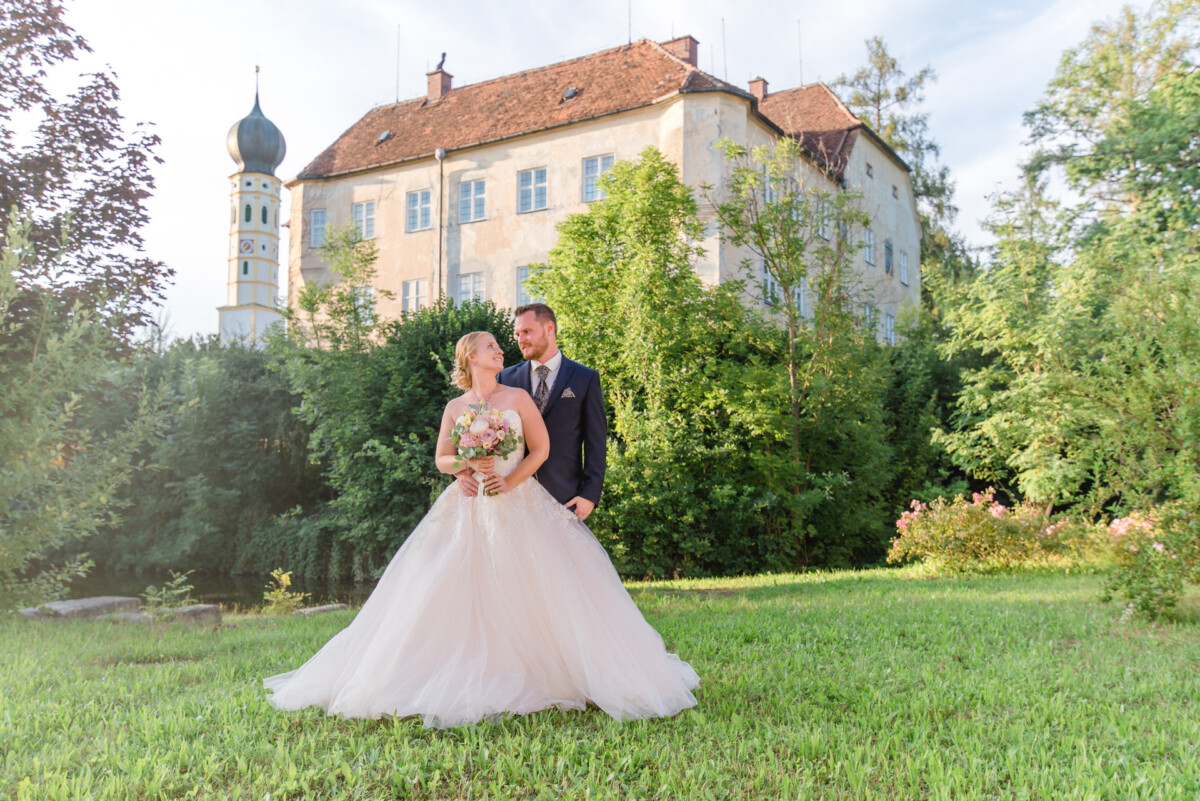 Natalie_Willi_Sulzemoos_00037 Ein Brautpaar steht vor einem Gebäude.