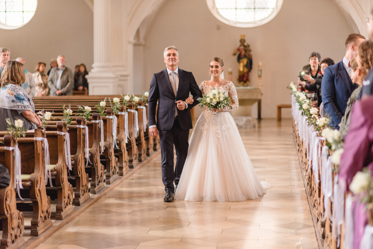 Sophia_Riccardo_Ammersee_00003 Ein Brautpaar, das den Gang einer Kirche hinuntergeht.