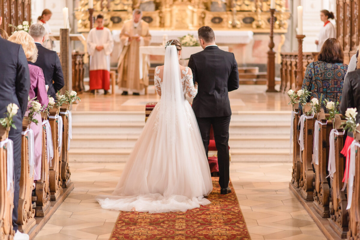 Sophia_Riccardo_Ammersee_00005 Ein Brautpaar, das den Gang einer Kirche hinuntergeht.