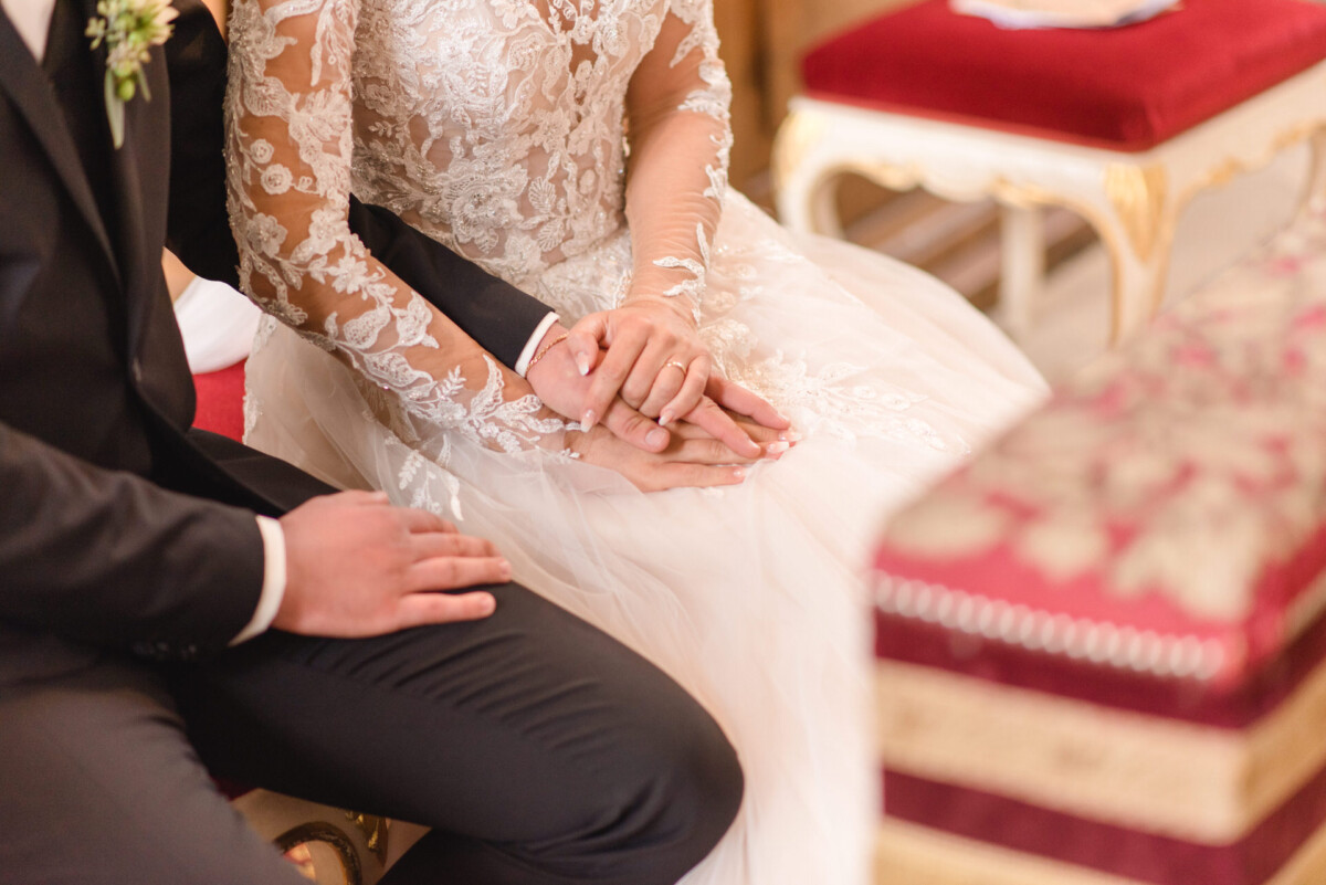 Sophia_Riccardo_Ammersee_00011 Ein Brautpaar hält Händchen in einer Kirche.