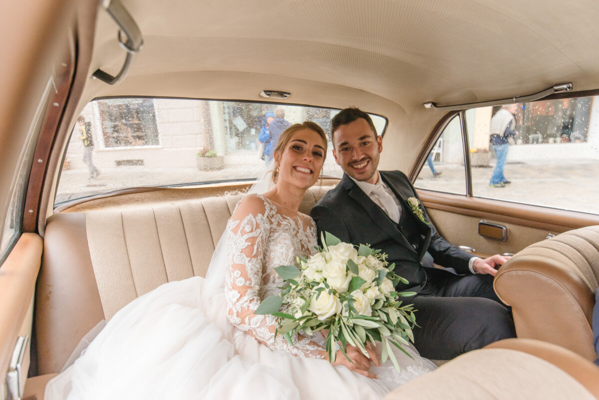 Sophia_Riccardo_Ammersee_00017 Eine Braut und ein Bräutigam, die hinten in einem Auto sitzen.