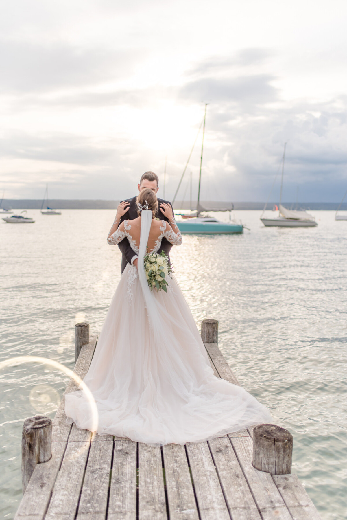 Sophia_Riccardo_Ammersee_00026 Eine Braut und ein Bräutigam stehen auf einem Dock.