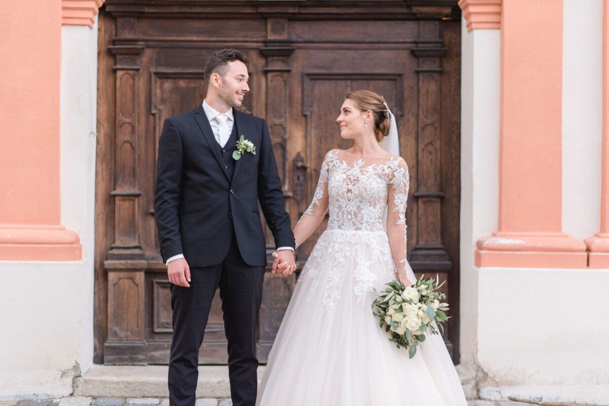 Sophia_Riccardo_Ammersee_00031 Ein Brautpaar steht vor einer Holztür.