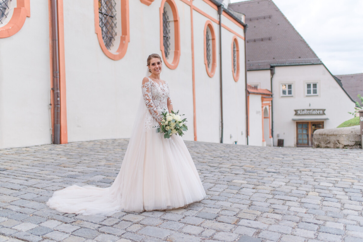 Sophia_Riccardo_Ammersee_00032 Eine Frau in einem Hochzeitskleid steht vor einem Gebäude.