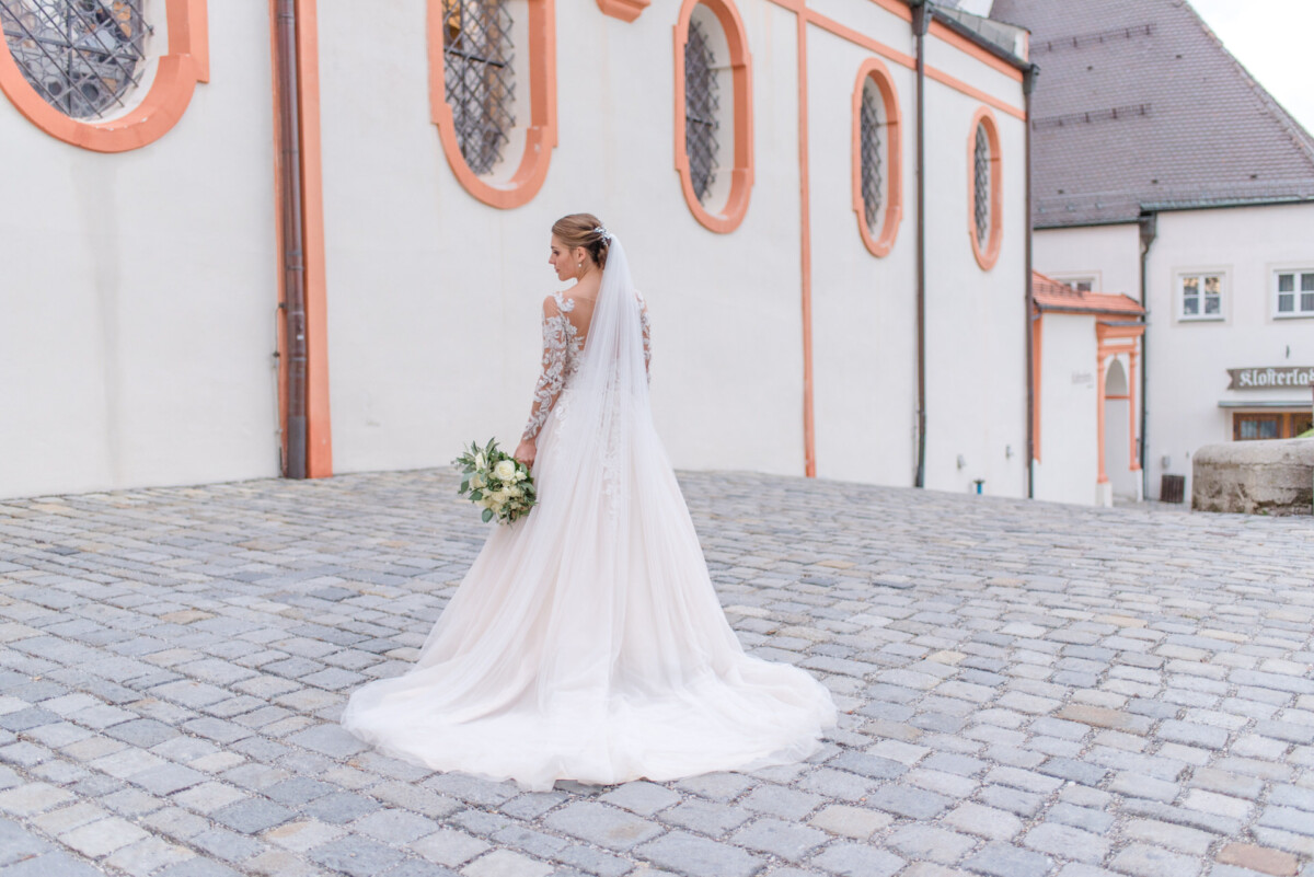Sophia_Riccardo_Ammersee_00036 Eine Frau in einem Hochzeitskleid steht vor einem Gebäude.
