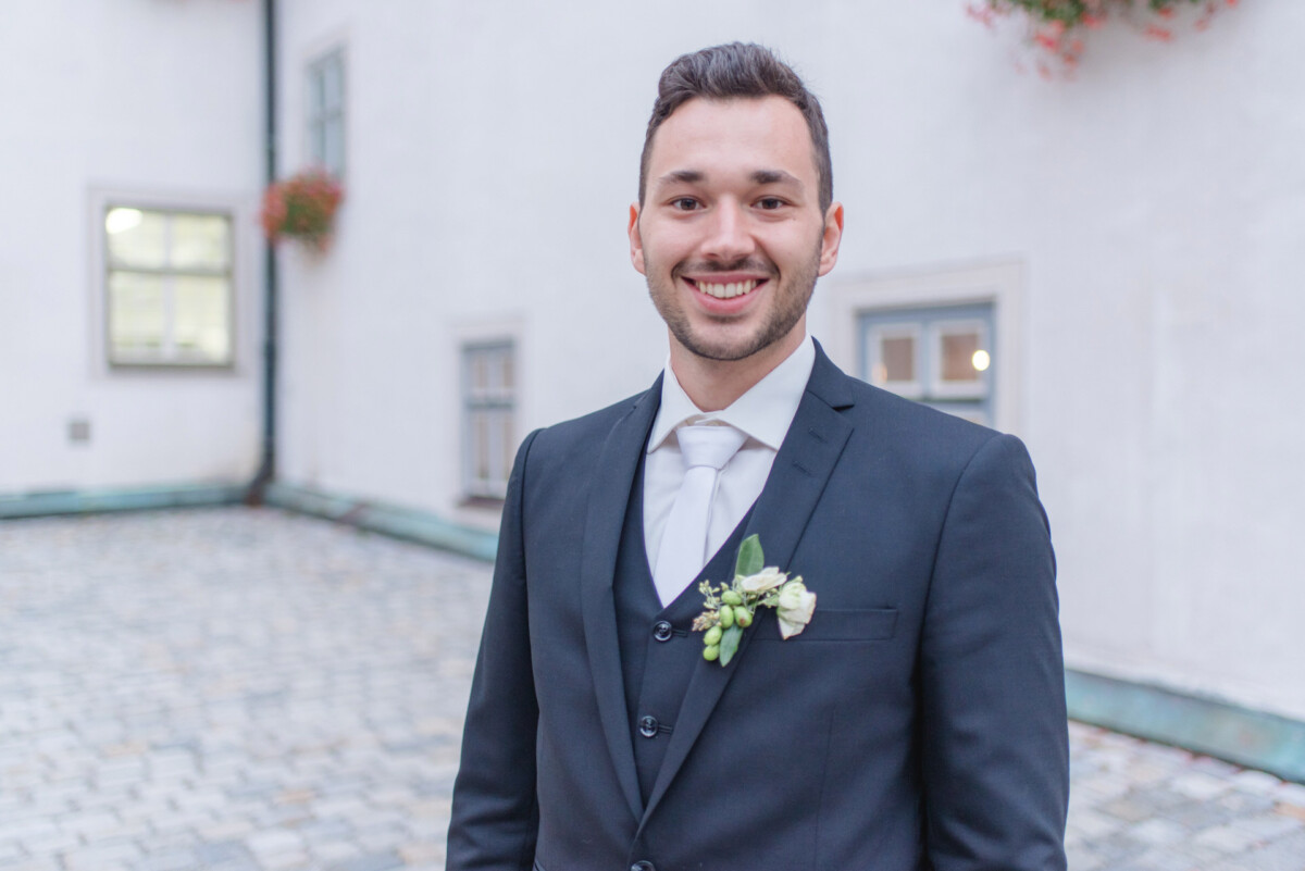 Sophia_Riccardo_Ammersee_00038 Ein Mann in Anzug und Krawatte steht vor einem Gebäude.