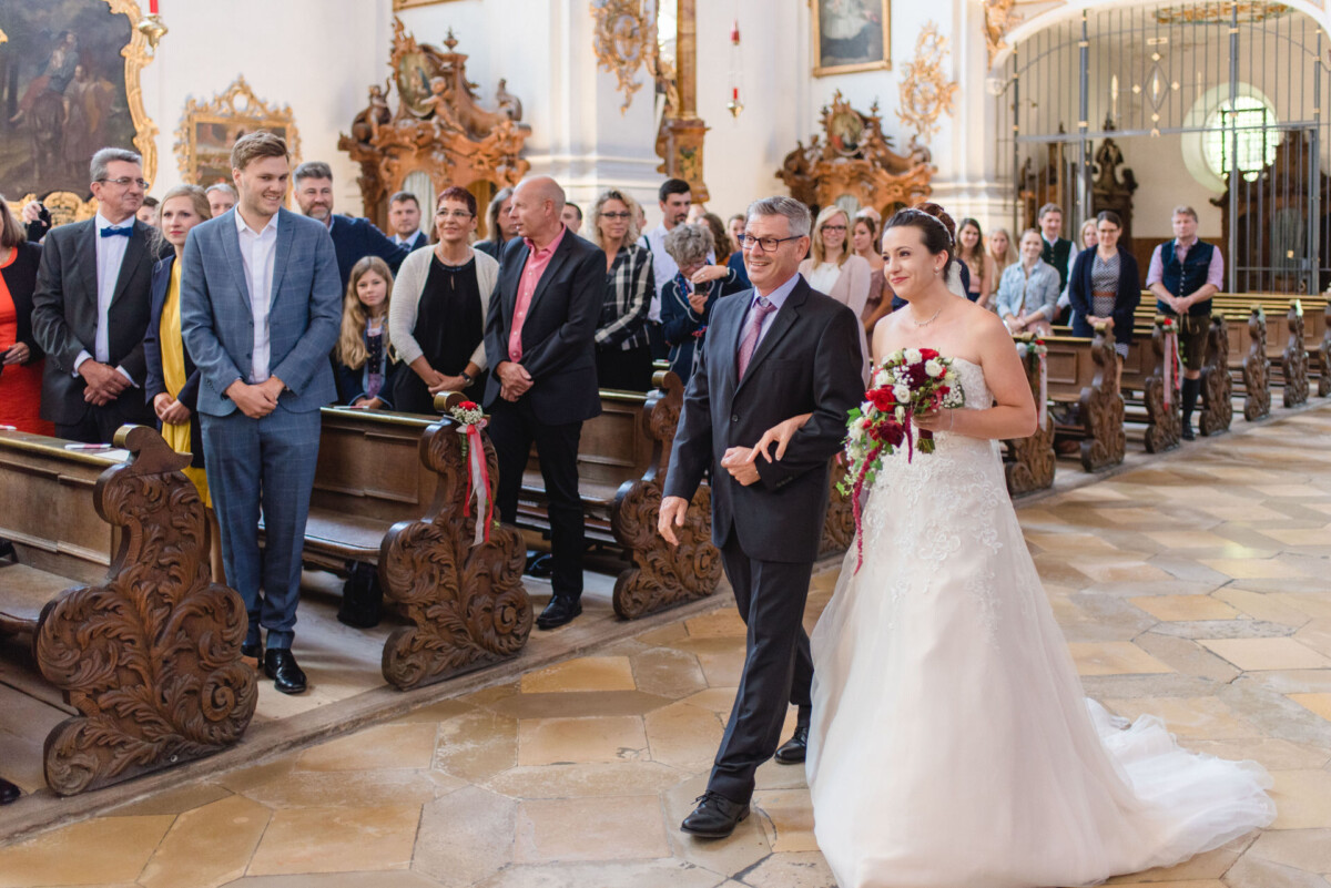 Stephi_Manu_Landsberg_am_Lech_00001 Ein Brautpaar, das den Gang einer Kirche hinuntergeht.