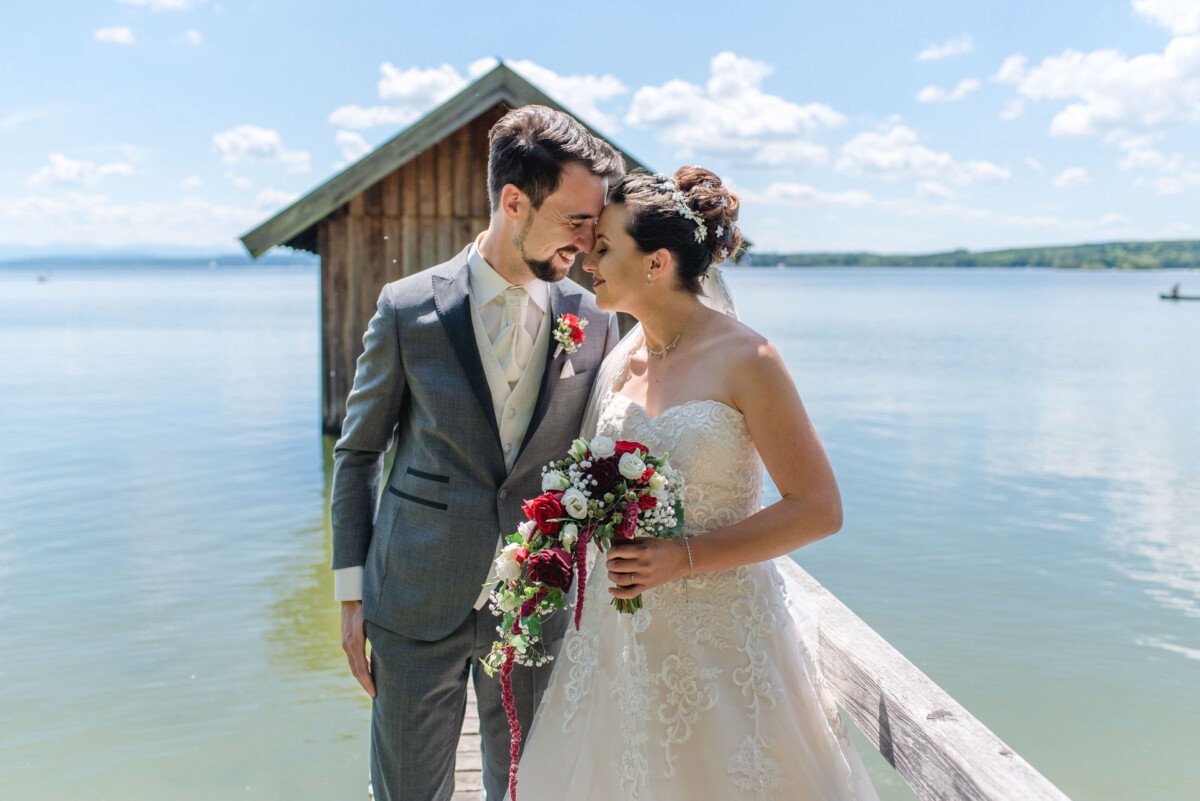 Stephi_Manu_Landsberg_am_Lech_00010 Eine Braut und ein Bräutigam, die auf einem Dock neben einem See stehen.