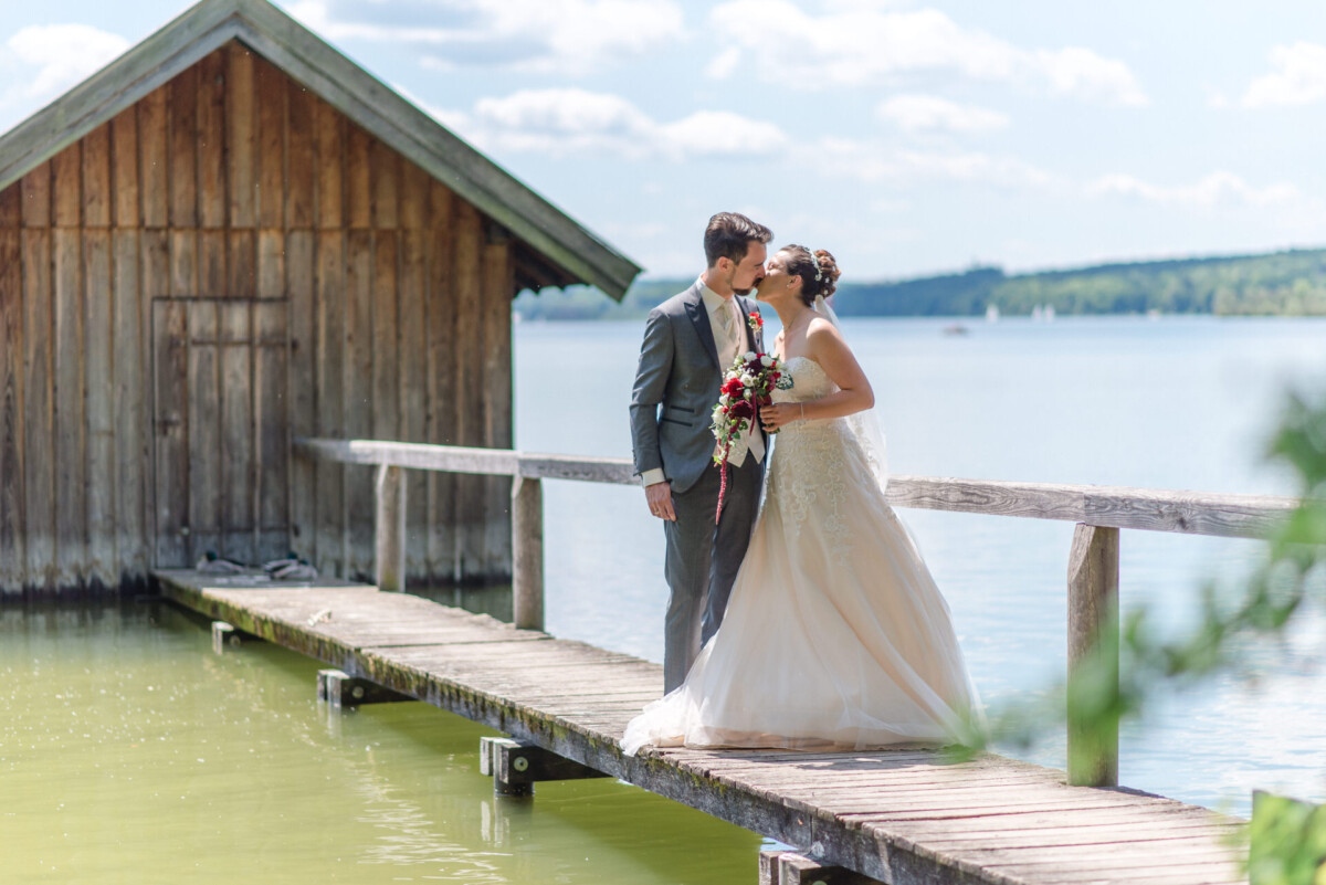 Stephi_Manu_Landsberg_am_Lech_00011 Eine Braut und ein Bräutigam, die auf einem Dock neben einem See stehen.