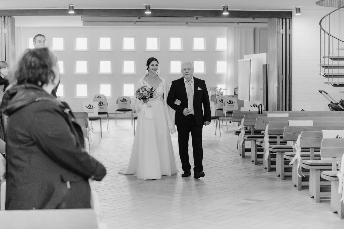 R_M_Bobingen_Langerringen_Hochzeit_00059_web Ein Brautpaar, das den Gang einer Kirche hinuntergeht.