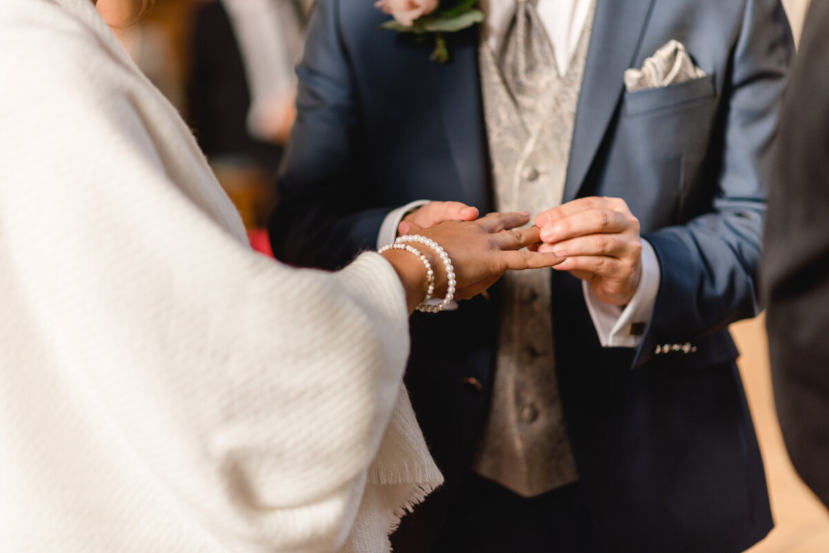 R_M_Bobingen_Langerringen_Hochzeit_00121_web Ein Mann und eine Frau, die während einer Hochzeitszeremonie Händchen halten.