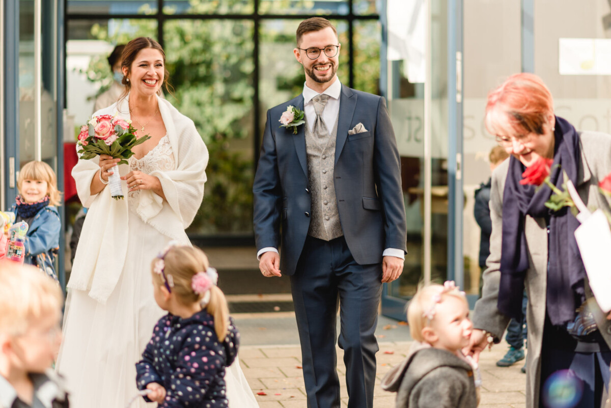 R_M_Bobingen_Langerringen_Hochzeit_00192_web Eine Braut und ein Bräutigam gehen mit ihren Kindern den Gang entlang.