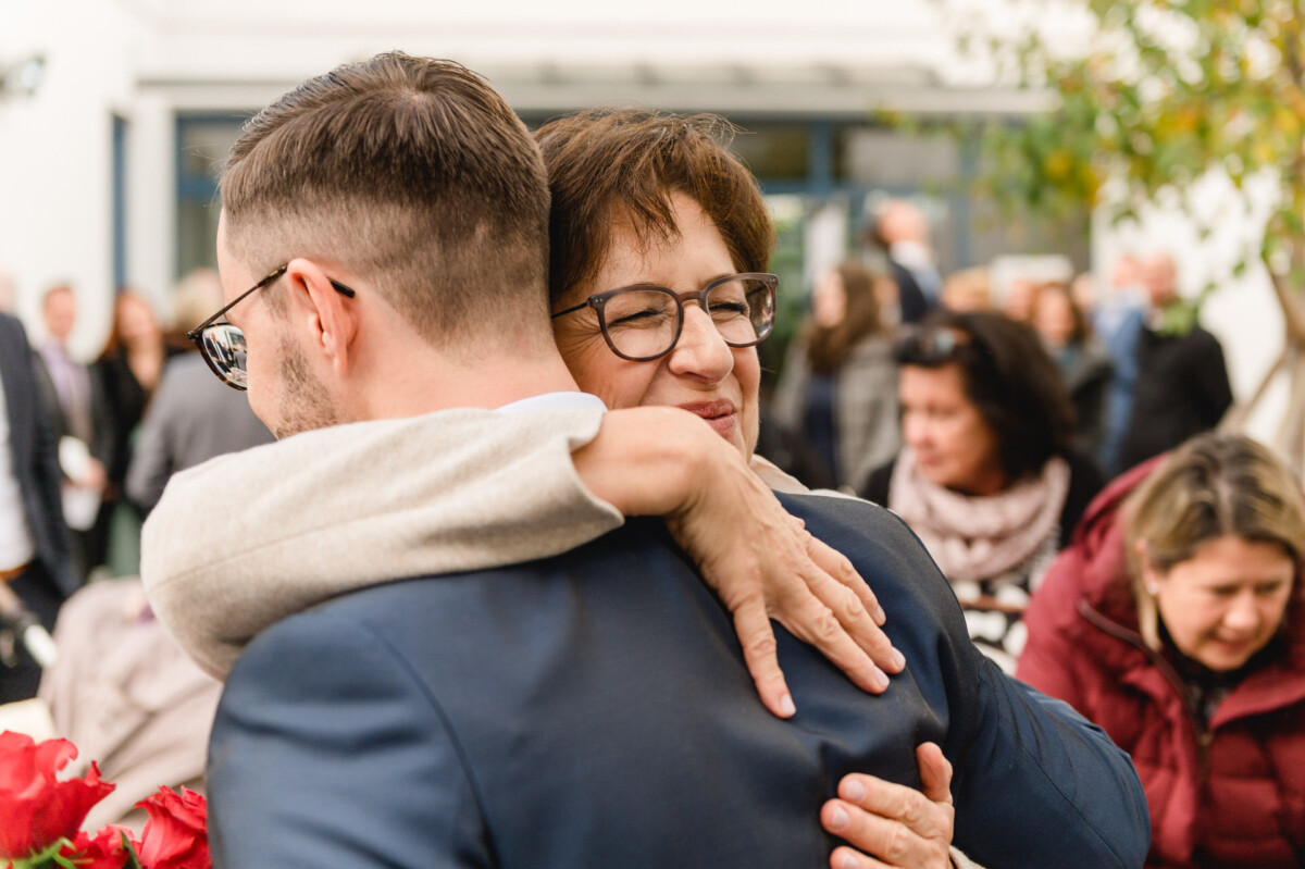 R_M_Bobingen_Langerringen_Hochzeit_00246_web Ein Mann umarmt eine Frau in einer Menschenmenge.