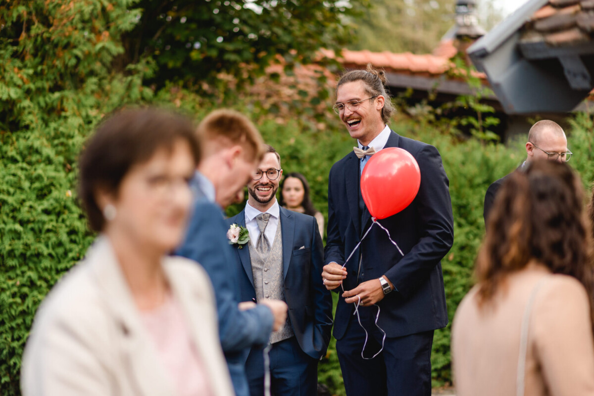 R_M_Bobingen_Langerringen_Hochzeit_00405_web ein Mann in einem Anzug, der einen roten Luftballon hält.