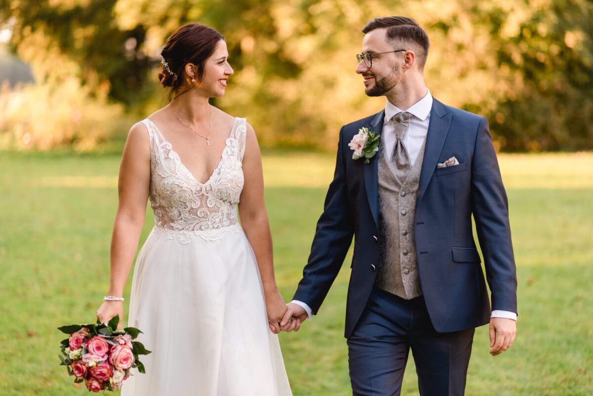 Eine Braut und ein Bräutigam halten Händchen in einem Feld.