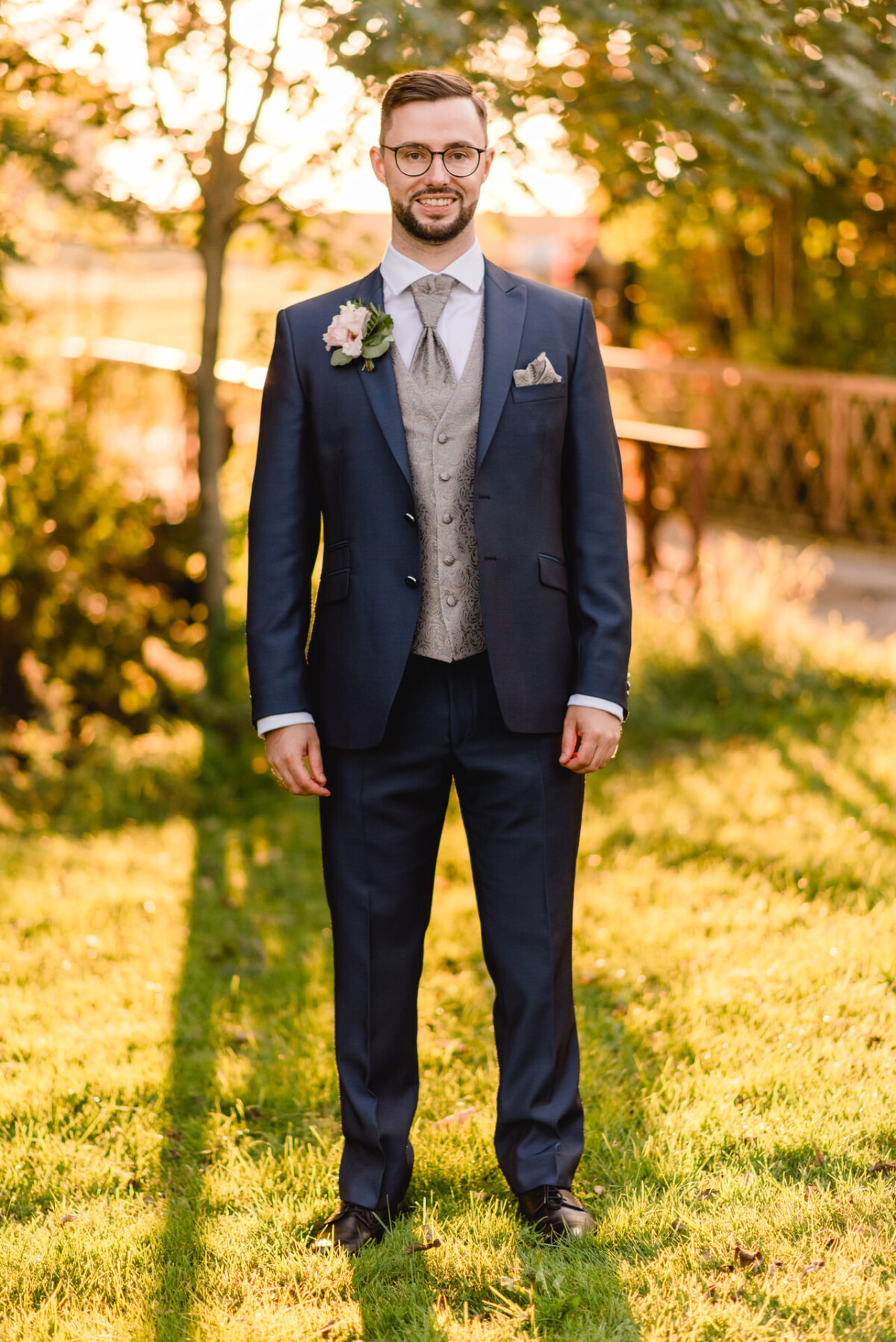 R_M_Bobingen_Langerringen_Hochzeit_00742_web Ein Bräutigam im Anzug steht im Gras.