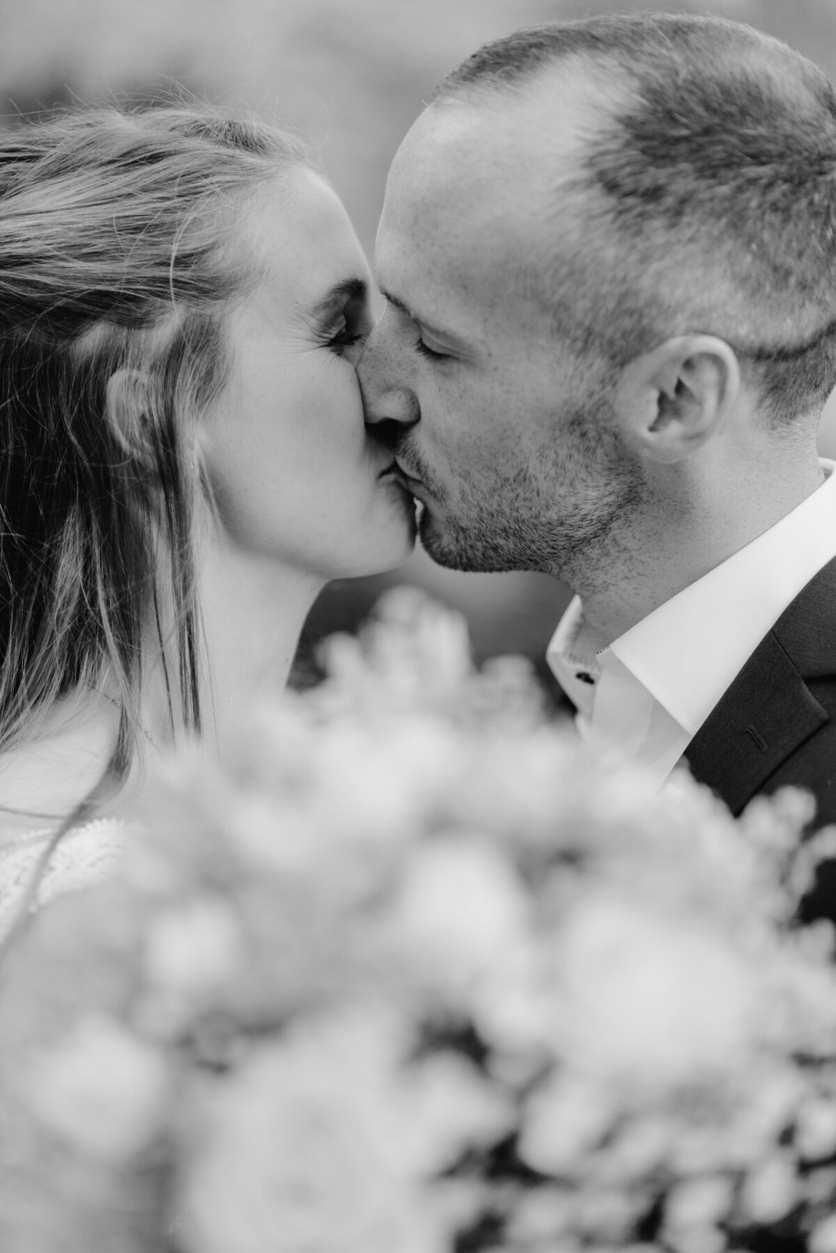 ein Brautpaar, das sich vor einem Blumenstrauß küsst.