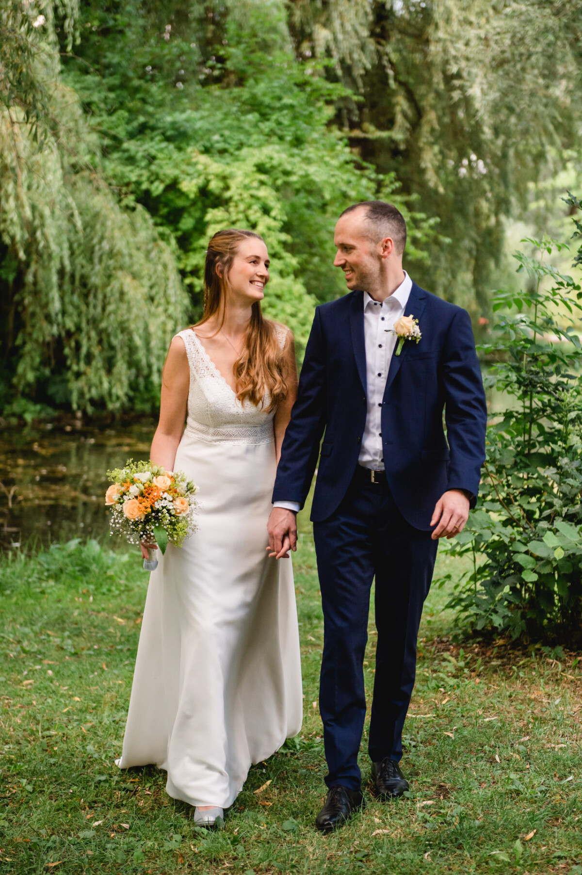 eine Braut und ein Bräutigam, die zusammen im Gras spazieren gehen.