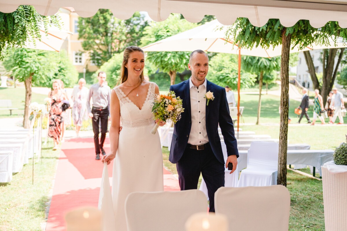 eine Braut und ein Bräutigam, die einen Gang mit rotem Teppich hinuntergehen.