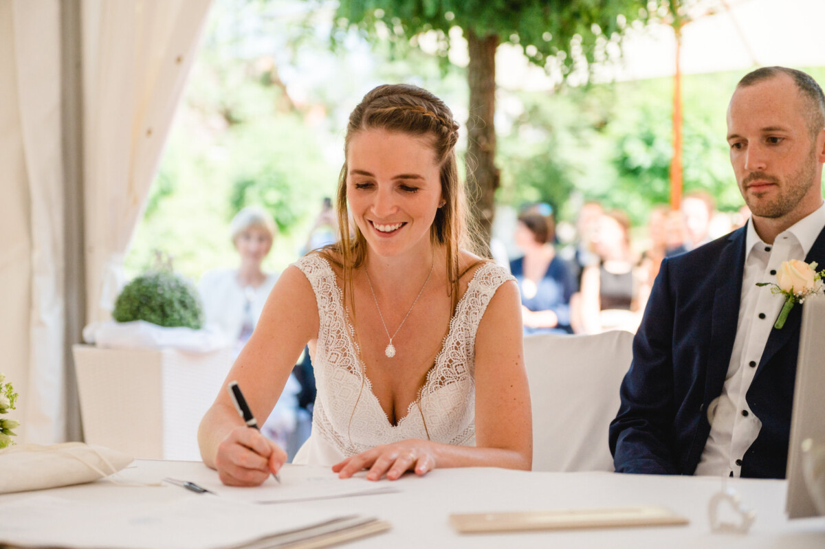 eine Braut und ein Bräutigamu sitzen an einem Tisch und unterschreiben Papiere.