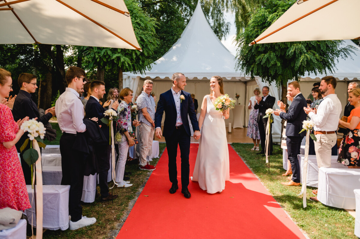 eine Braut und ein Bräutigam, die einen Gang mit rotem Teppich hinuntergehen.