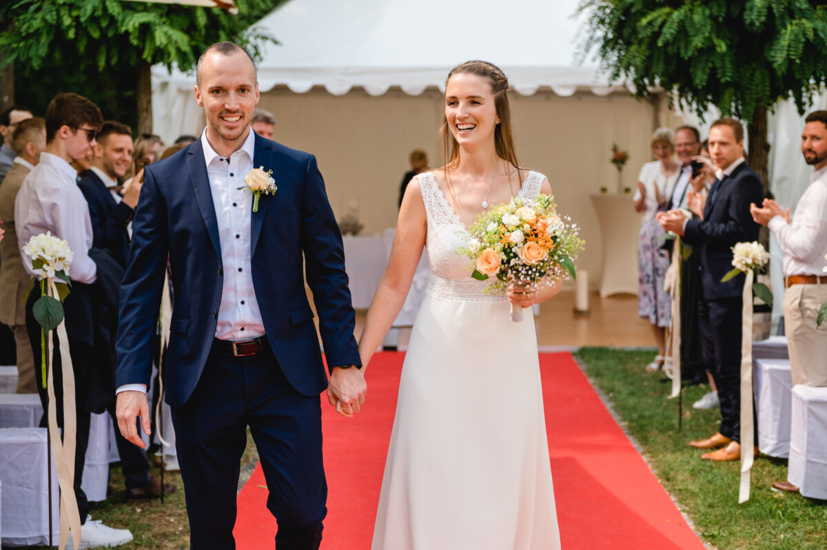 Ein Bräutigam und eine Braut gehen einen Gang mit rotem Teppich entlang.