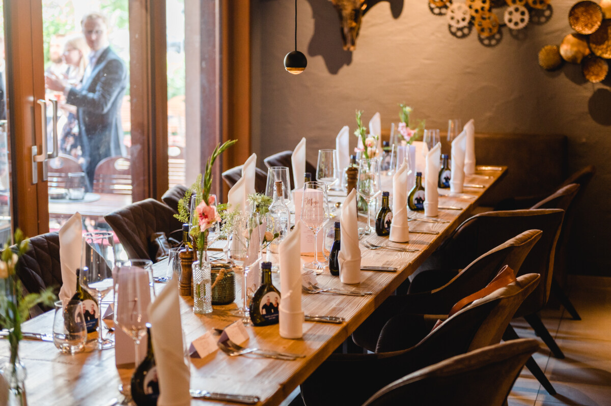 ein langer Holztisch mit Weinflaschen und Gläsern darauf.