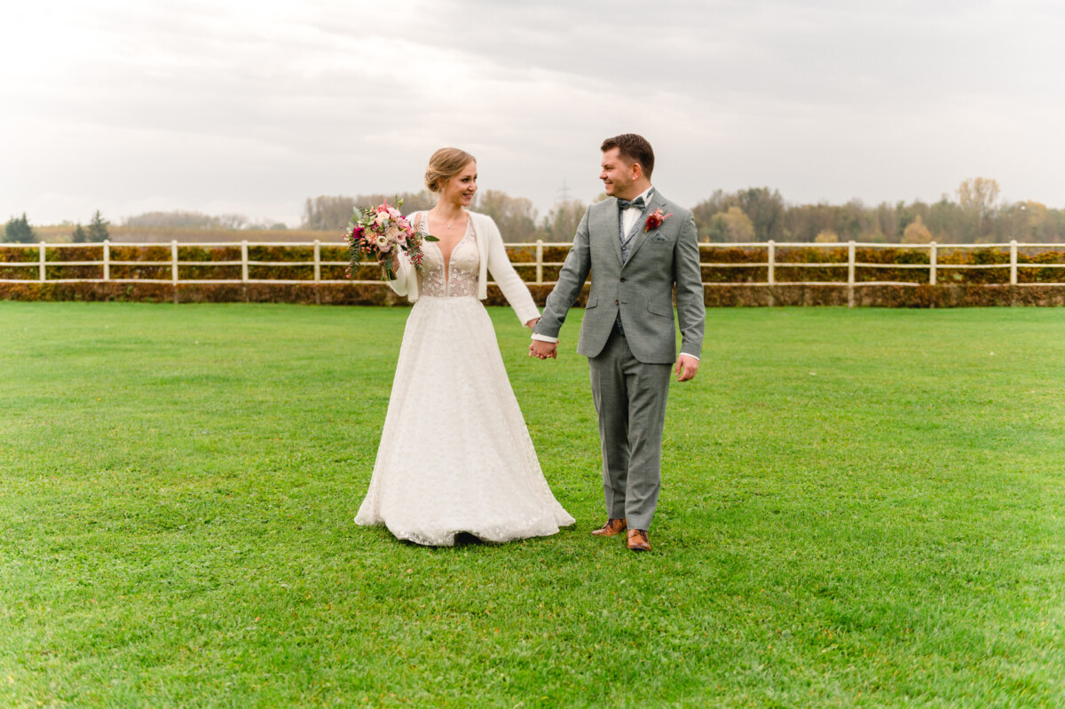 Eine Braut und ein Bräutigam halten Händchen in einem Feld.
