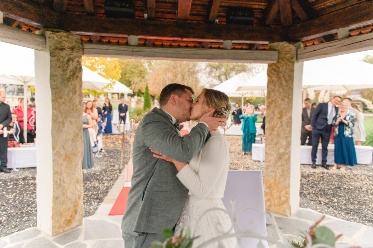 ein Brautpaar, das sich unter einem Pavillon küsst.