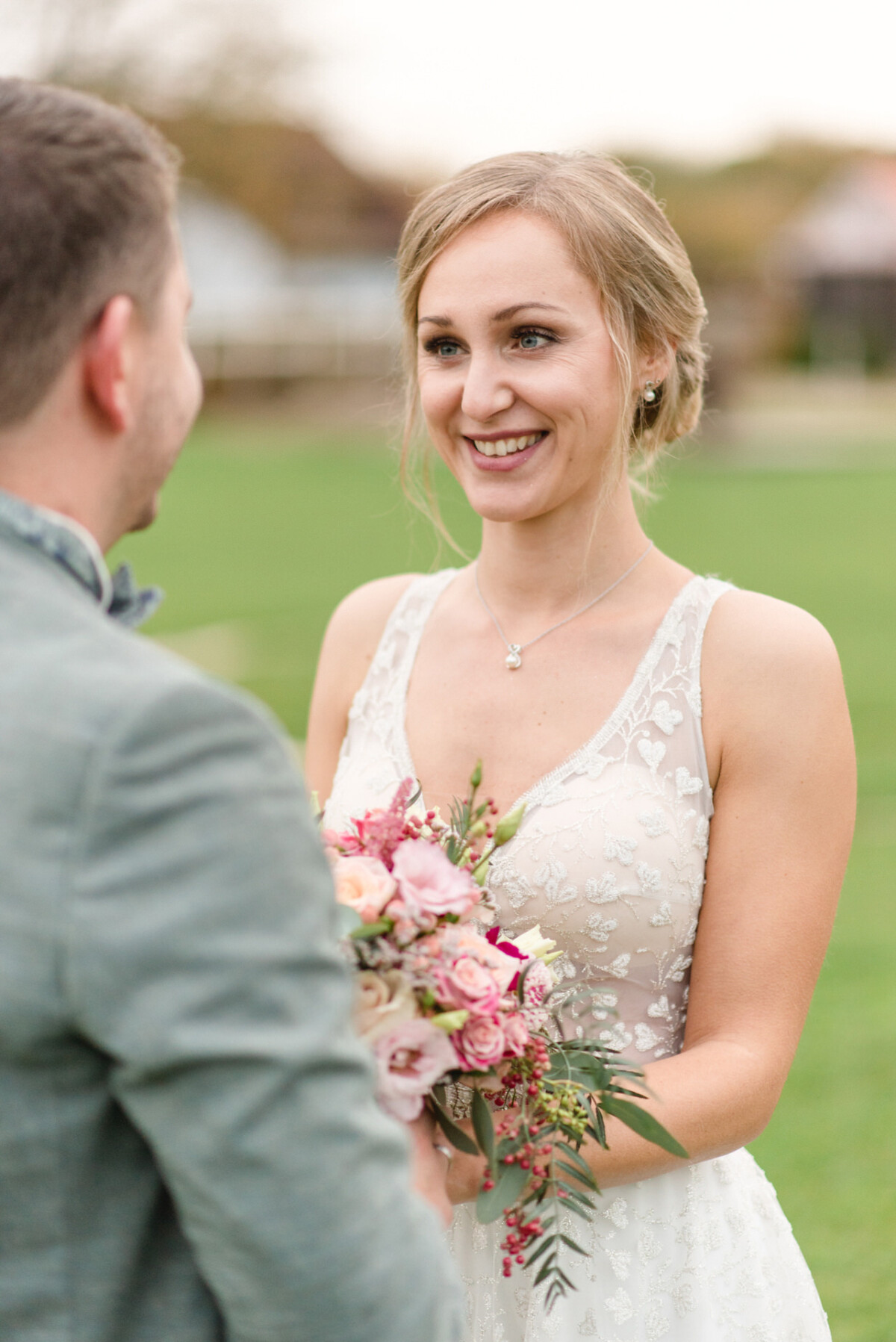 Eine Braut und ein Bräutigam lächeln einander auf einem Feld an.
