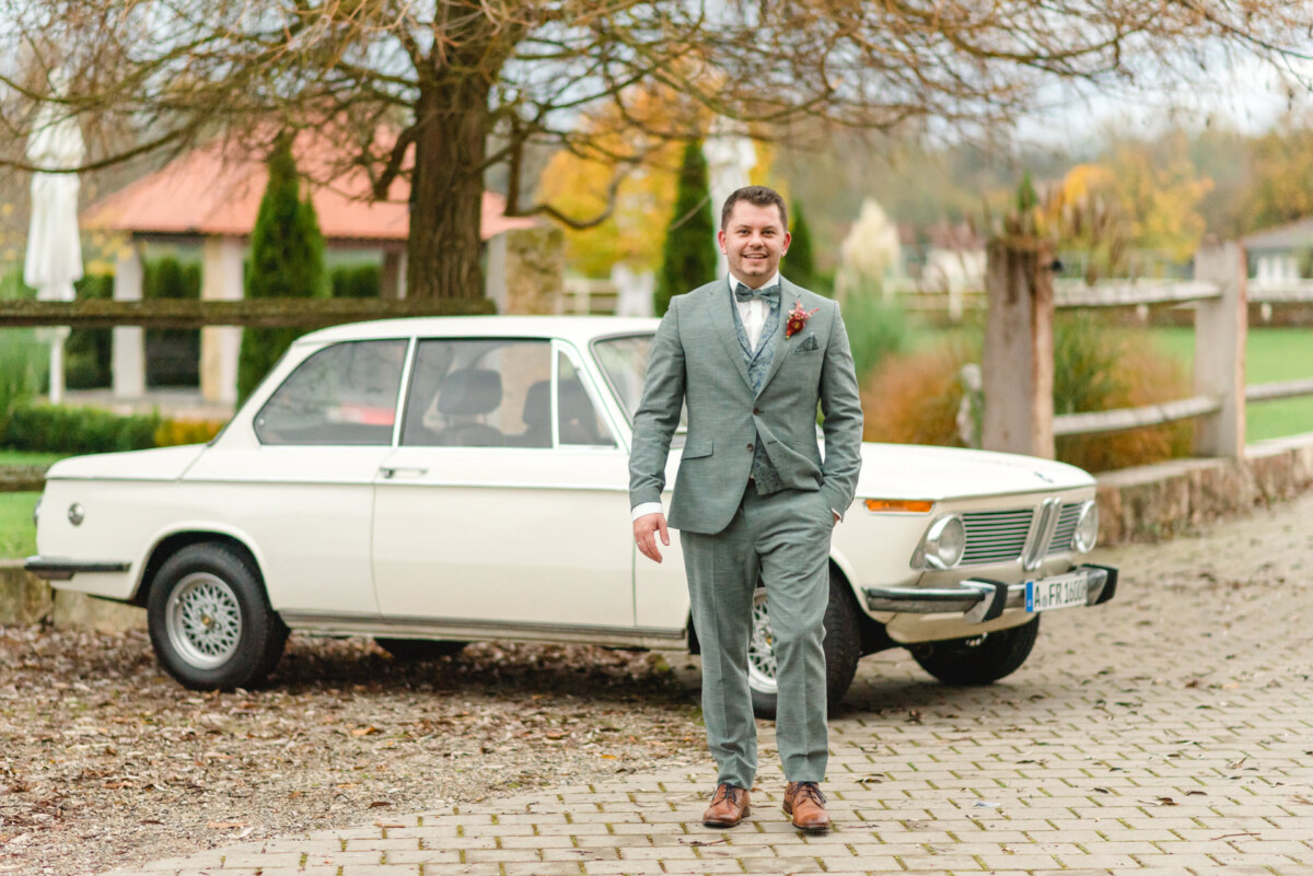 Ein Bräutigam im Anzug steht neben einem Oldtimer im Land-Steakhaus Bürger in Marxheim.